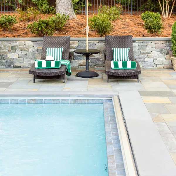 two wicker lounge chairs sit between a sitting wall and underground fiberglass pool